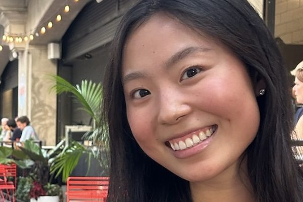 Kayla Chang, a women with long brown hair, smiling in front of a building.